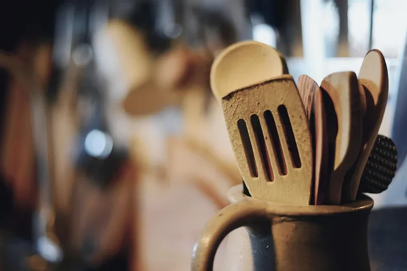 Wooden spoons and spatulas standing in a ceramic crock on a kitchen counter