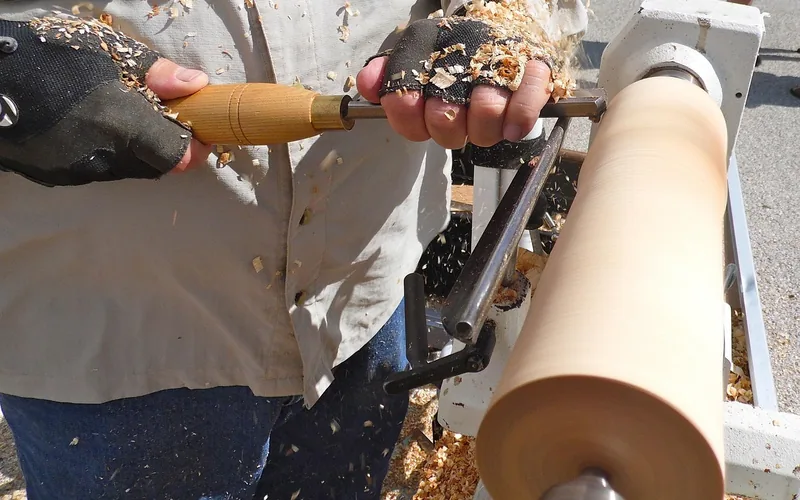 Woodworker turning lumber on a lathe with sawdust accumulating on gloves and clothing Woodworker turning lumber on a lathe with sawdust accumulating on gloves and clothing