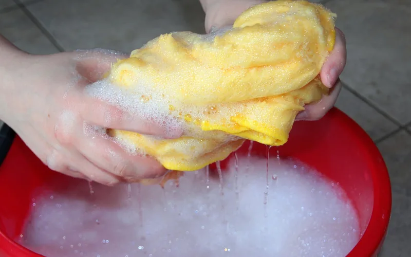 hands wringing out a soft soapy cloth over a bucket for cleaning wooden handles hands wringing out a soft soapy cloth over a bucket for cleaning wooden handles