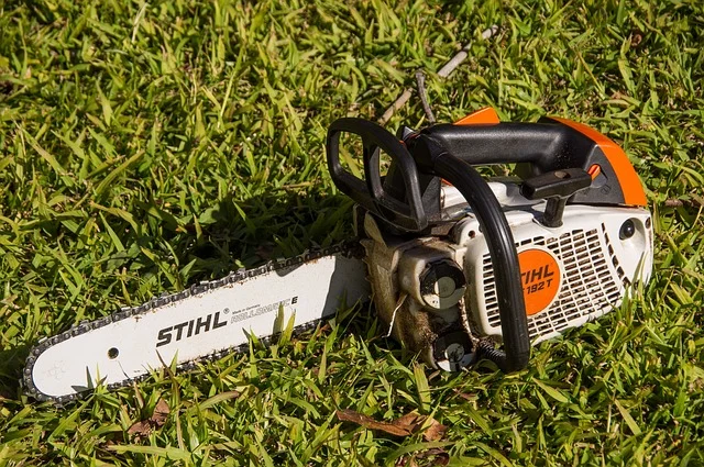 A Stihl gas chainsaw resting in grass, showing the orange and white body styling typical of the Farm and Ranch saw lineup