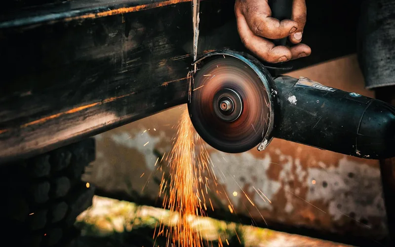 hand guiding an angle grinder cutoff wheel through a rusted metal beam