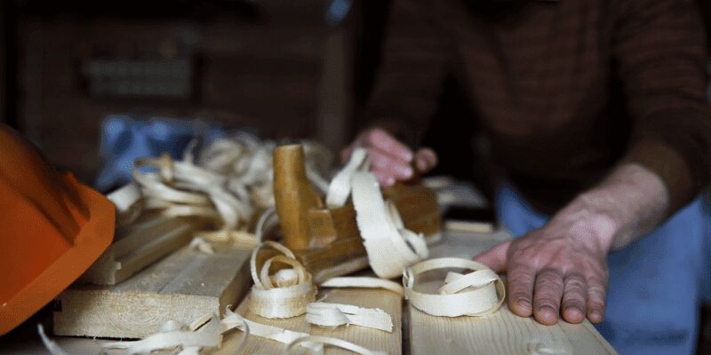 hand plane shavings curling off a board edge on a workbench