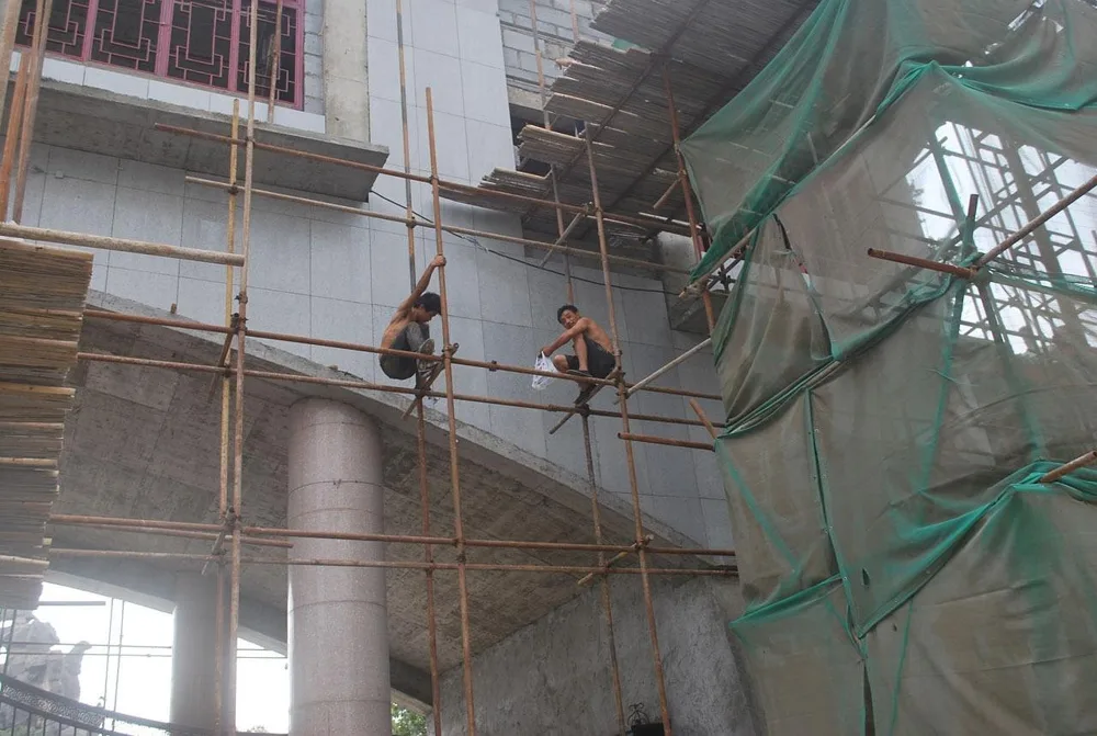 Workers on a bamboo scaffold lashed together beside a building under construction