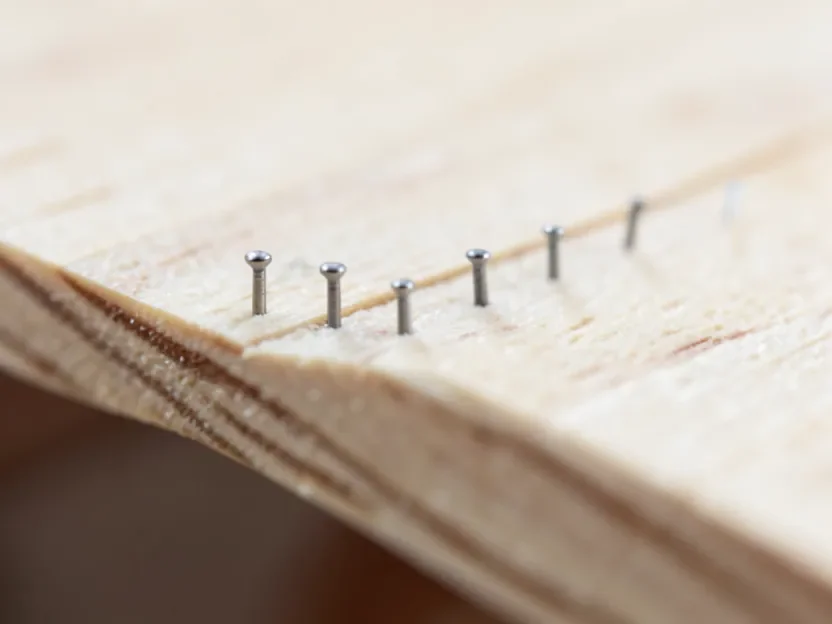 Row of 18-gauge brad nail heads driven flush into the edge of 1/4 inch plywood without splitting