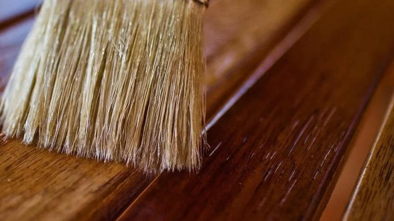 Natural bristle brush applying a glossy finish to warm brown wood slats