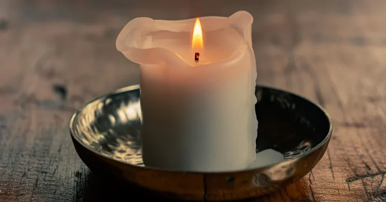 lit candle dripping melted wax onto a wood table surface