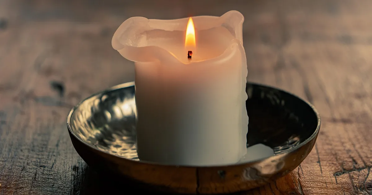 lit candle dripping melted wax onto a wood table surface
