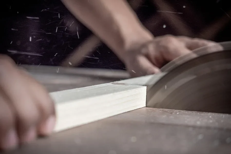 Carpenter feeding a board into a saw to cut lumber for a wooden cross