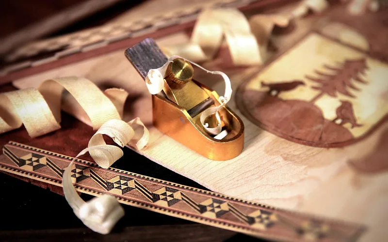 A small brass hand plane resting on a decorative wood veneer inlay strip with curled shavings A small brass hand plane resting on a decorative wood veneer inlay strip with curled shavings