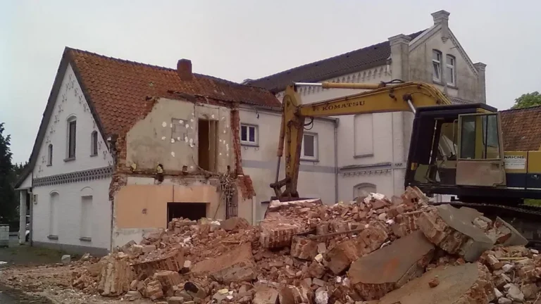 Partly demolished house with an excavator and a pile of brick rubble on a renovation site