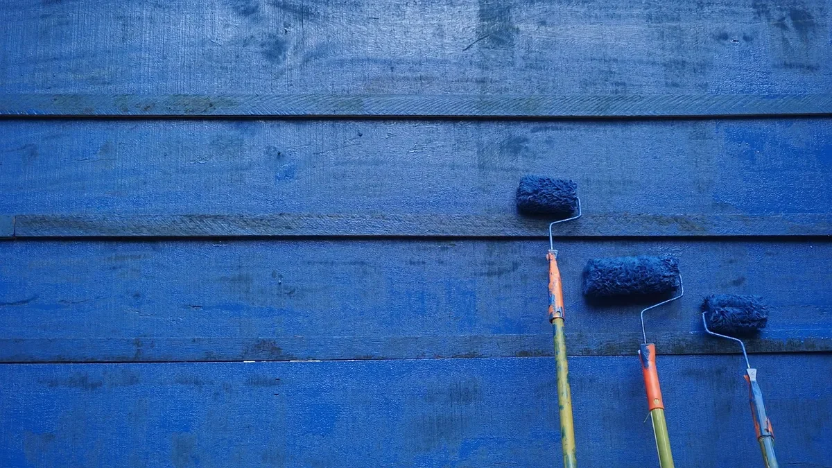 Blue painted wooden boards with three paint rollers leaning against them