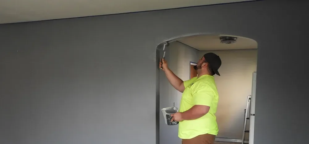 Painter rolling paint around a doorway arch after wall repairs were sanded smooth