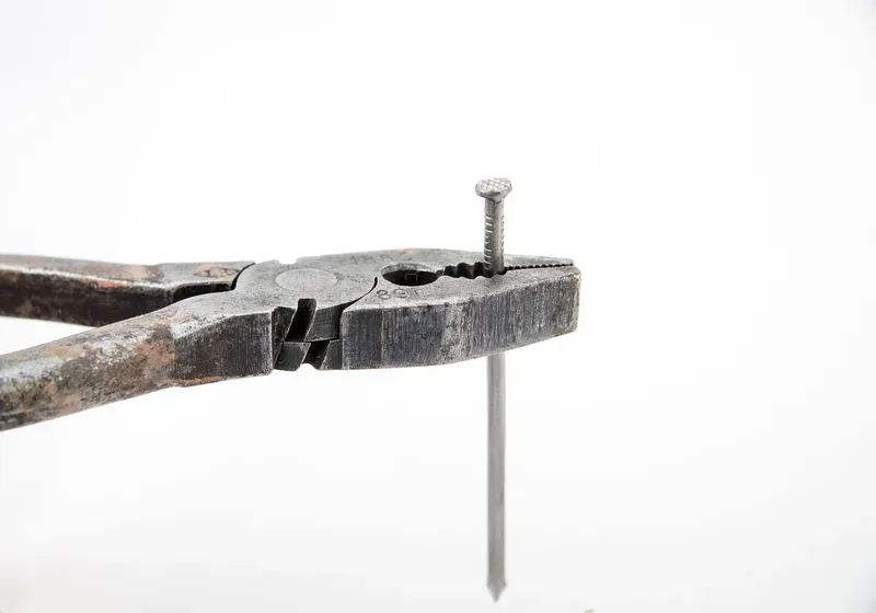 Pliers gripping a nail beside its cut-off shank