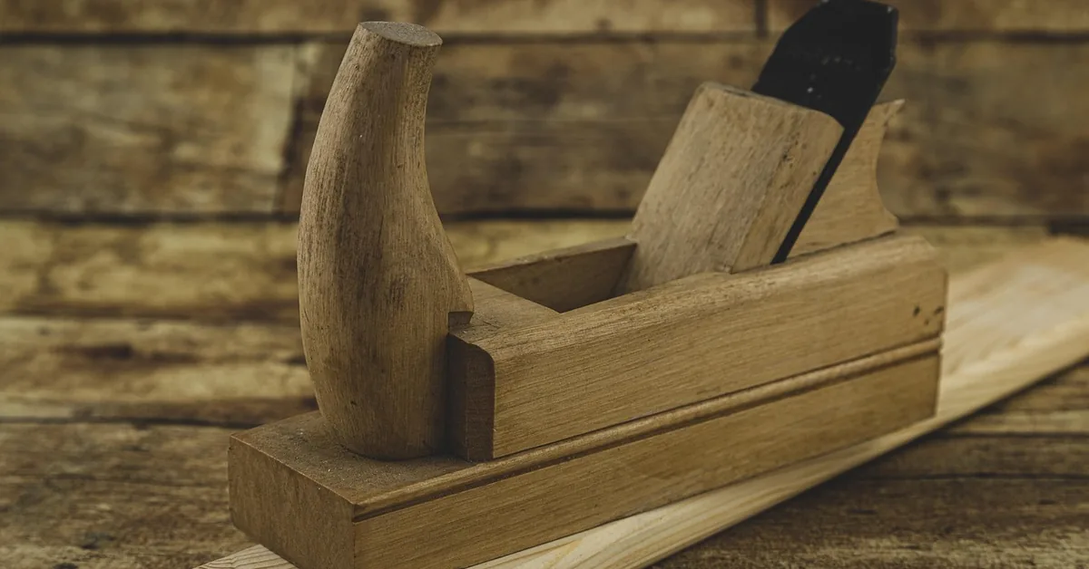 wooden hand plane resting on a pine board edge in a workshop
