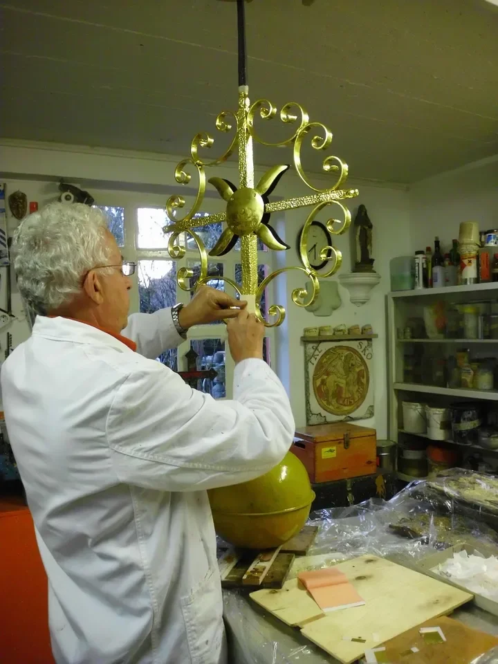 Gilder applying gold leaf to a decorative metal piece in a workshop