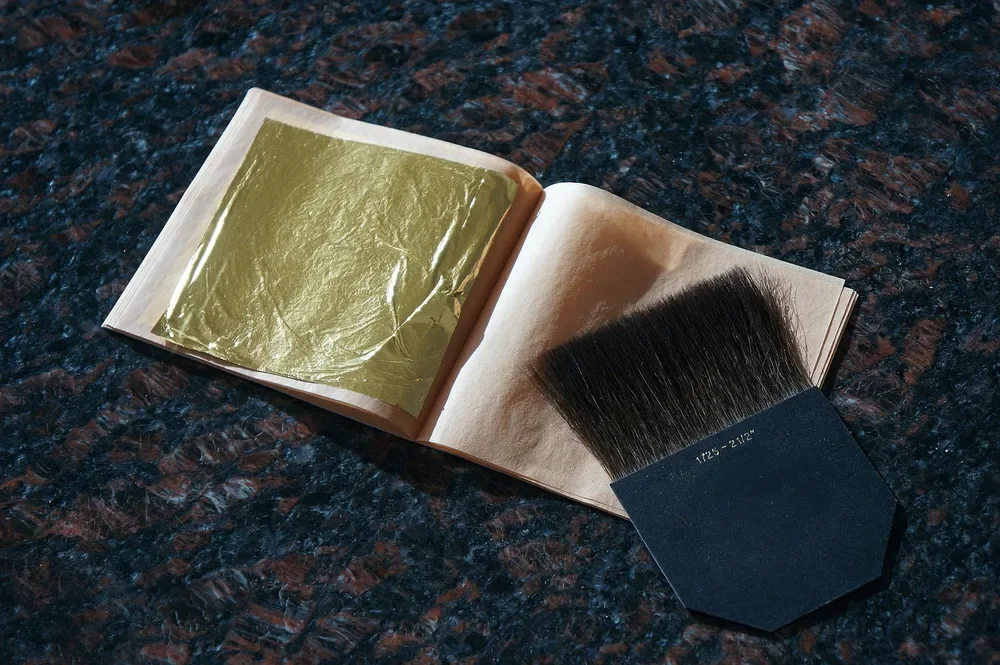 Book of loose gold leaf next to a gilder brush