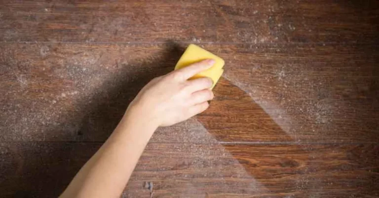 hand using yellow sponge to wipe a motor oil spill off a hardwood floor
