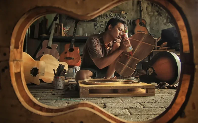 Craftsman applying adhesive to a wooden instrument part in a workshop