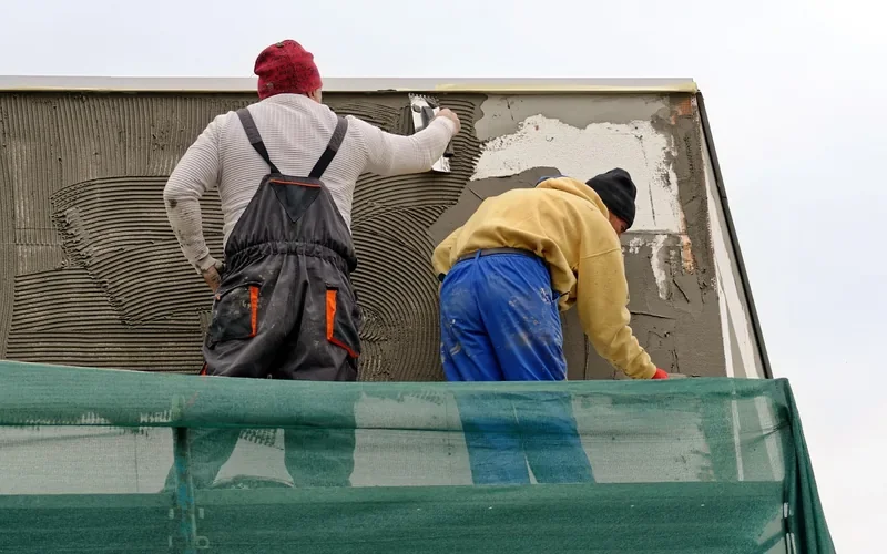 Worker spreading construction adhesive evenly with a notched trowel before setting a panel Worker spreading construction adhesive evenly with a notched trowel before setting a panel