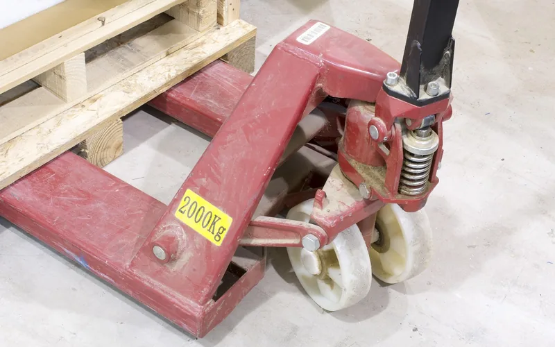 manual pallet jack positioned under a wooden pallet in a warehouse manual pallet jack positioned under a wooden pallet in a warehouse