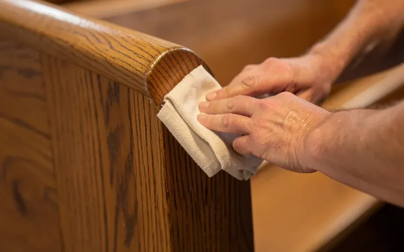 Hands applying wax polish with a soft cloth to a solid oak church pew armrest Hands applying wax polish with a soft cloth to a solid oak church pew armrest
