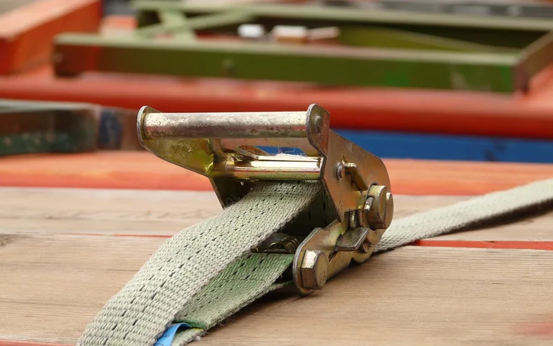 close-up of a ratchet strap buckle tensioned over a wood load
