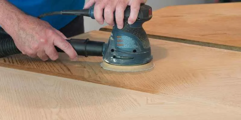 Person using an orbital sander to smooth a wood butcher block surface, removing old finish before oiling