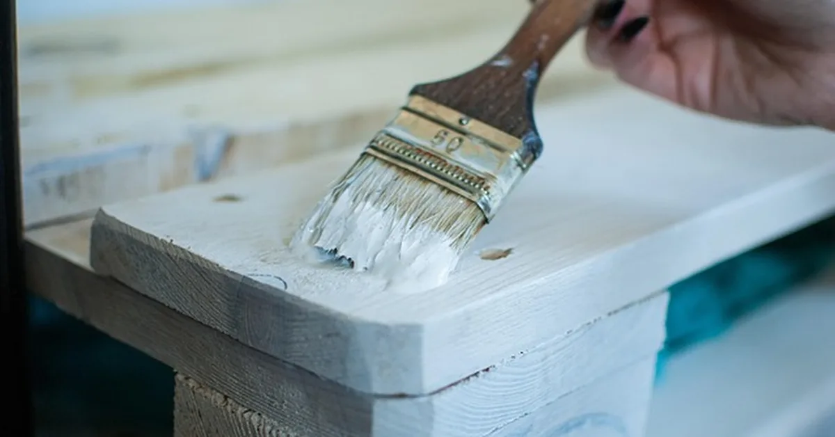 Applying white paint with a brush to a particle board furniture edge