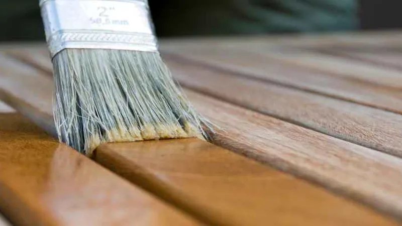 Close-up of a paintbrush applying wood stain along board slats