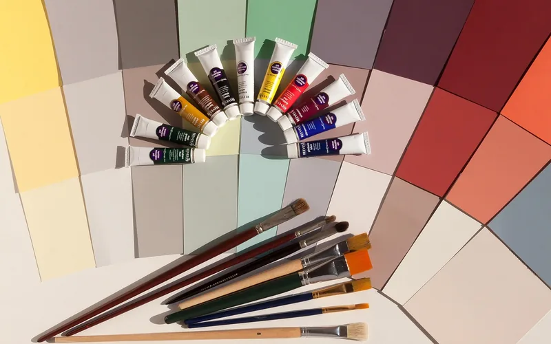 Paint color swatch cards fanned out with artist paint tubes and brushes for color matching