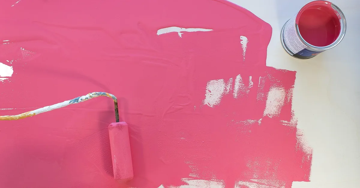 Roller applying freshly tinted pink paint next to an open tint base paint can
