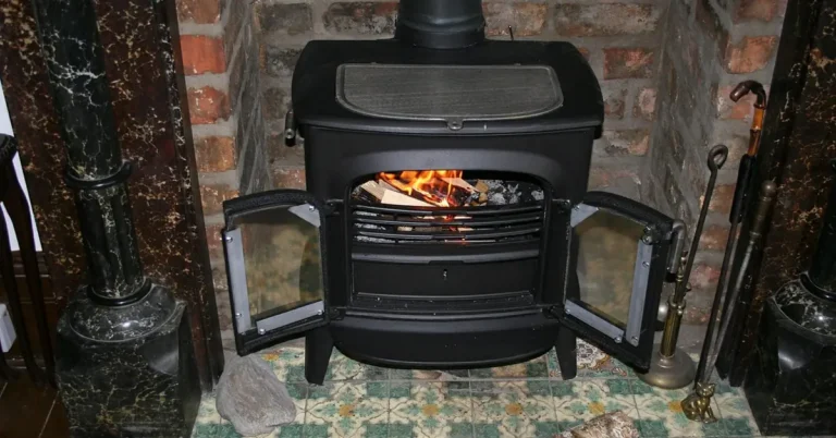 Wood-burning stove with the door open showing a lit fire and chimney flue pipe