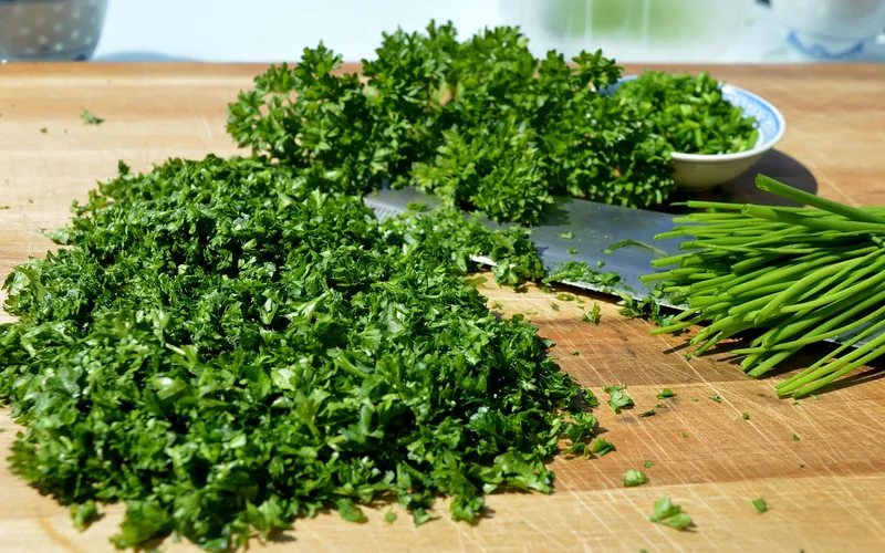 fresh herbs and chives chopped on a wood cutting board with a chef knife