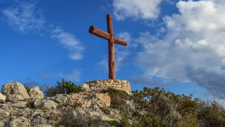 Tall wooden cross standing upright on a rocky hilltop against a blue sky
