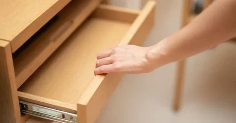 Hand opening a wooden dresser drawer with a wooden pull to access the screws underneath
