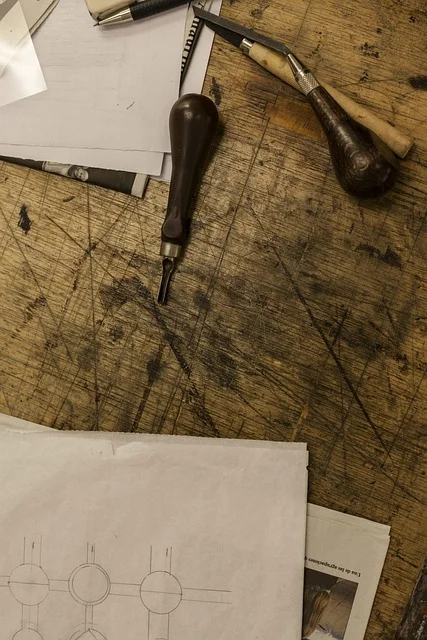Carving tools laid on a workbench beside a hand-drawn wooden weapon design sketch