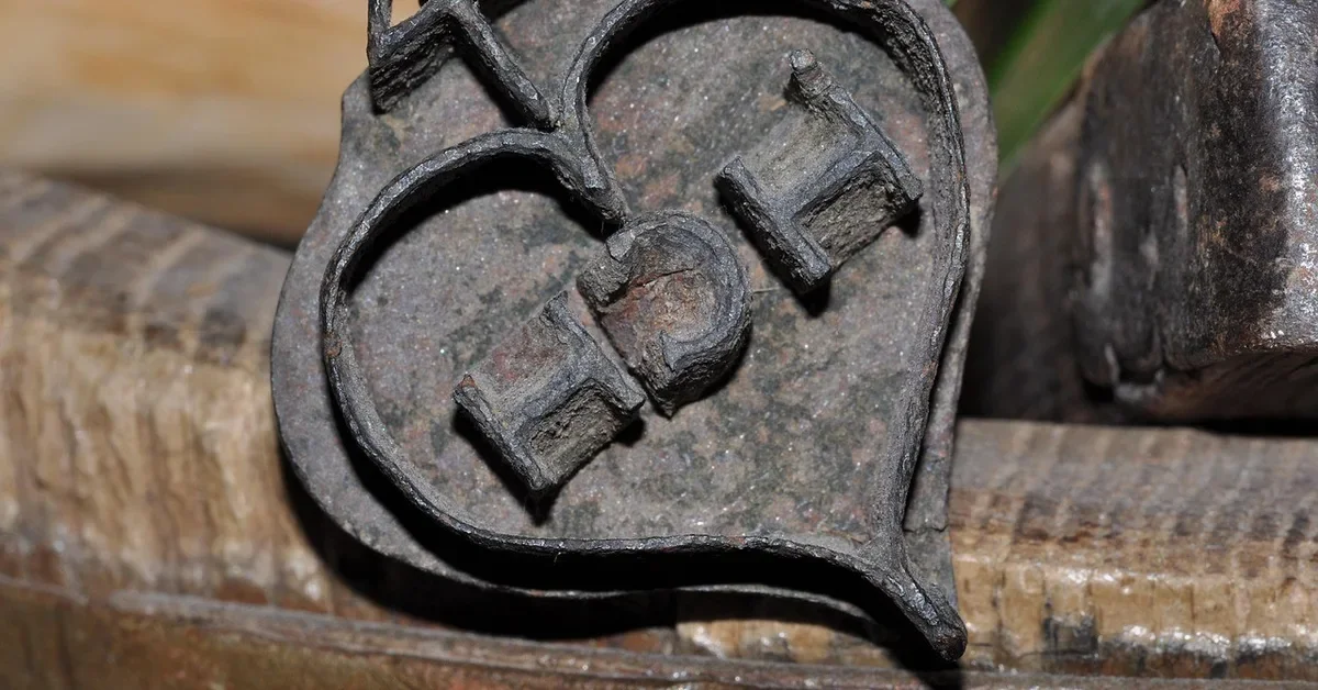 Antique iron brand with a heart-shaped maker mark resting against old wood