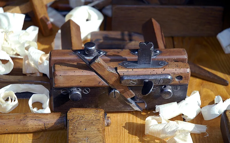 antique wood plow plane with metal fittings surrounded by wood shavings on a workbench