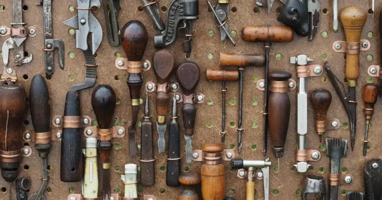 Wall of antique hand tools with several wooden-handled awls hanging on a pegboard
