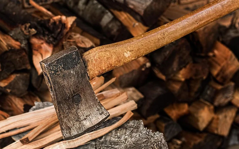 axe resting on a split firewood log with kindling in front of a stacked woodpile