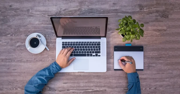 designer using a laptop and graphics tablet on a wooden desk to plan a woodworking project