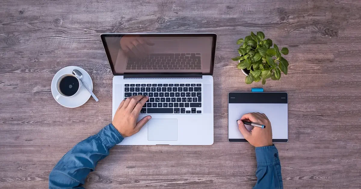 designer using a laptop and graphics tablet on a wooden desk to plan a woodworking project