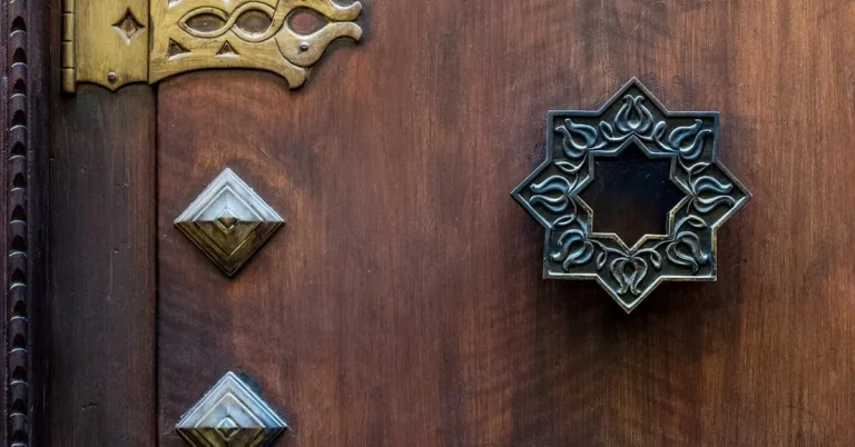 Close-up of a stained solid wood exterior door with brass strap hinge and decorative handle