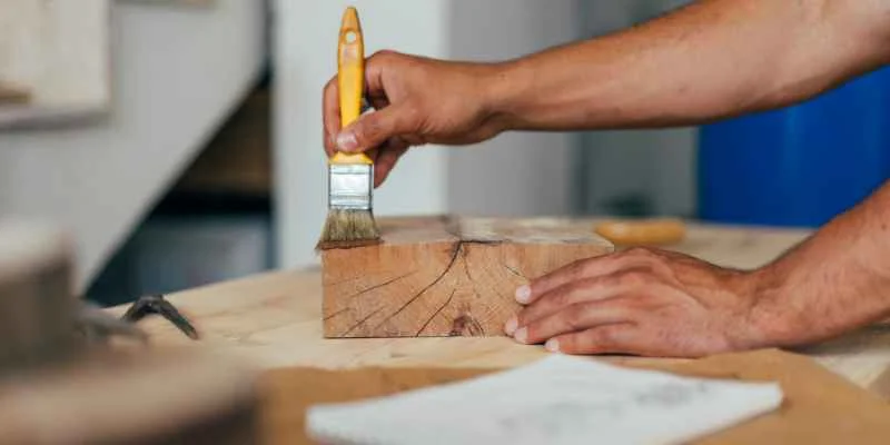 hand brushing wood stain onto a raw wood block with a paintbrush hand brushing wood stain onto a raw wood block with a paintbrush