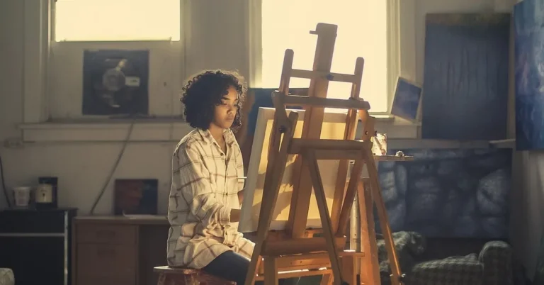 Artist painting on a stretched canvas at a wooden easel in a studio