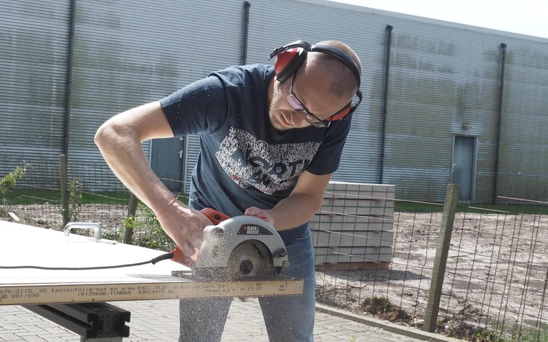 man wearing safety glasses and ear protection using a handheld circular saw outdoors
