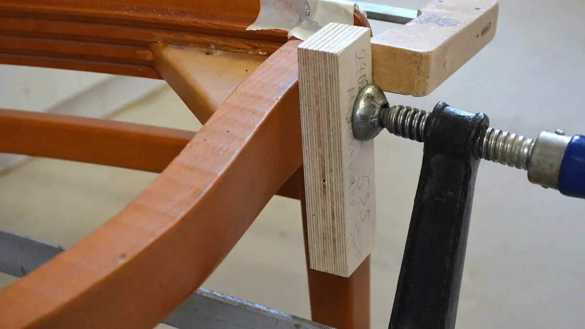 Bar clamp holding a glued wooden chair frame joint while it dries