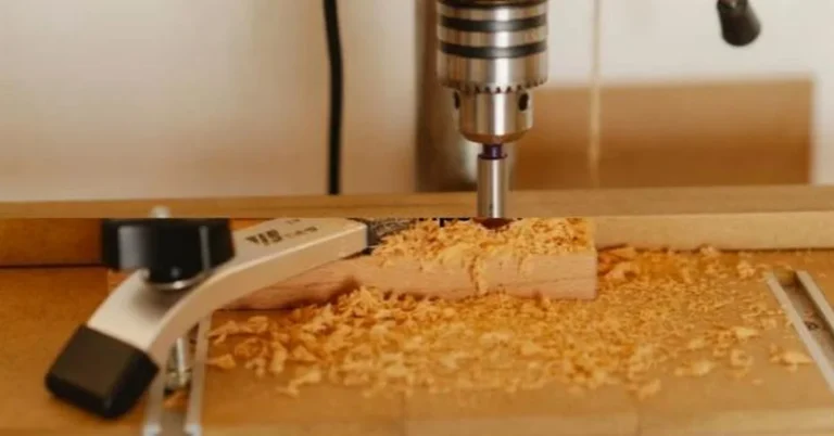 Drill press bit boring into clamped wood with shavings scattered around