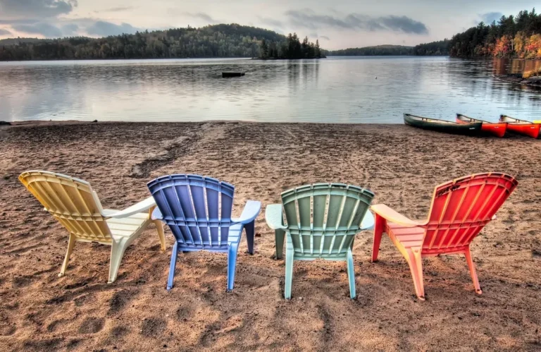 Four colorful resin Adirondack chairs facing a lake at dusk