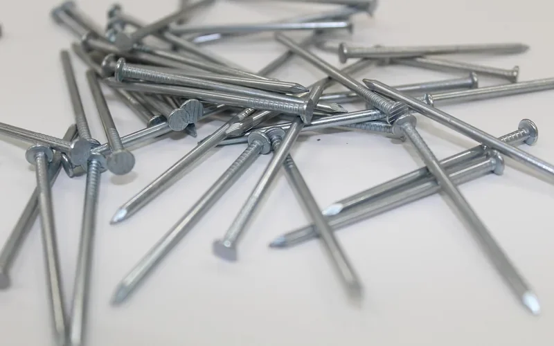 Pile of flat-headed steel nails on a white surface Pile of flat-headed steel nails on a white surface
